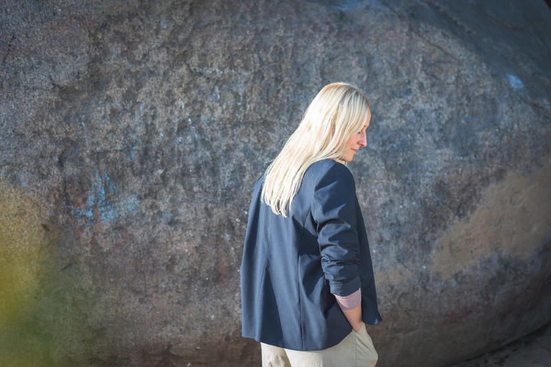 Frau steht vor einer Steinwand mit dem R&uuml;cken zur Kamera